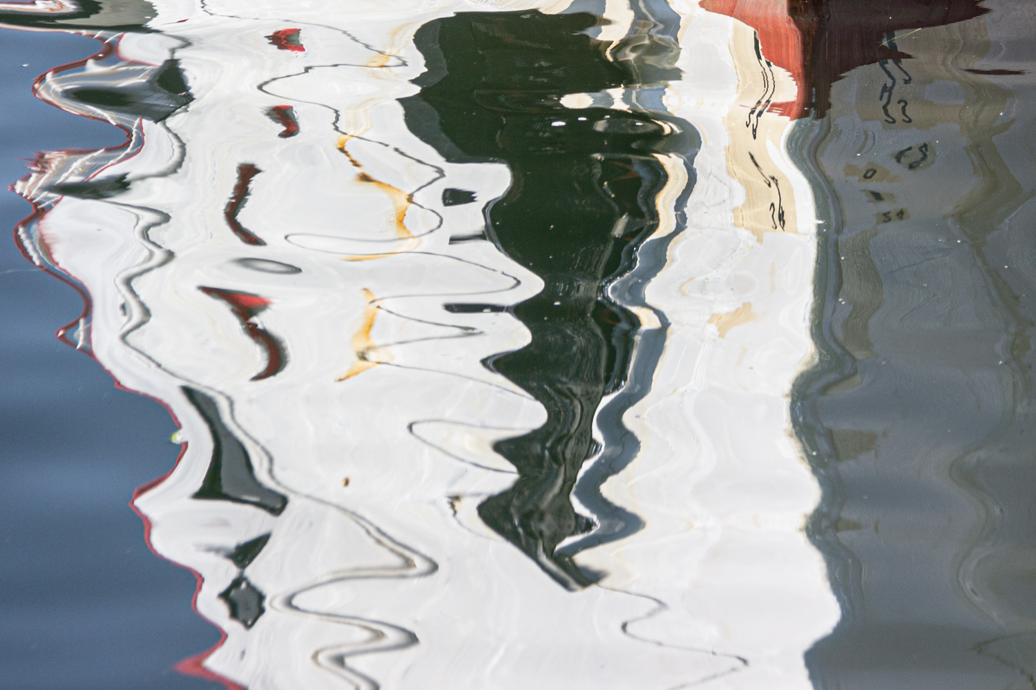Ein Schiffsrumpf spiegelt sich im Wasser am Kieler Hafen