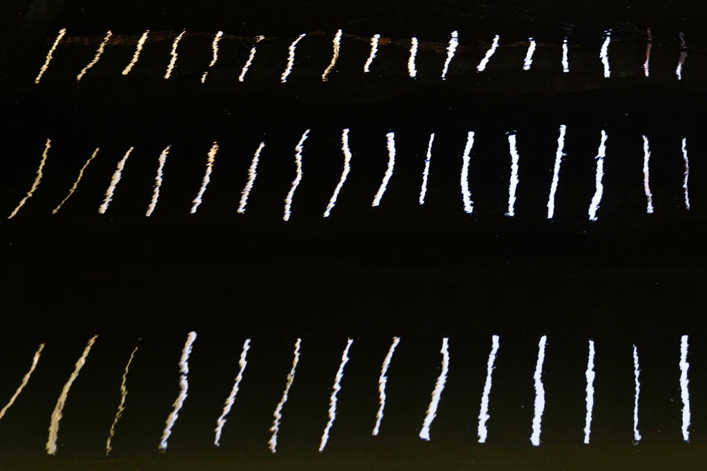 Licht fällt durch die Fugen eines Holz-Steges übder dem Wasser